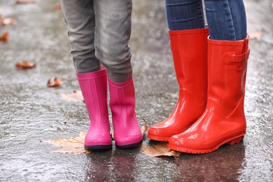 Photo of Mother and daughter wearing rubber boots after rain, focus of legs. Autumn walk