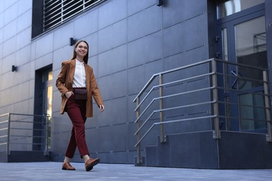 Young woman in formal clothes walking near building outdoors, space for text