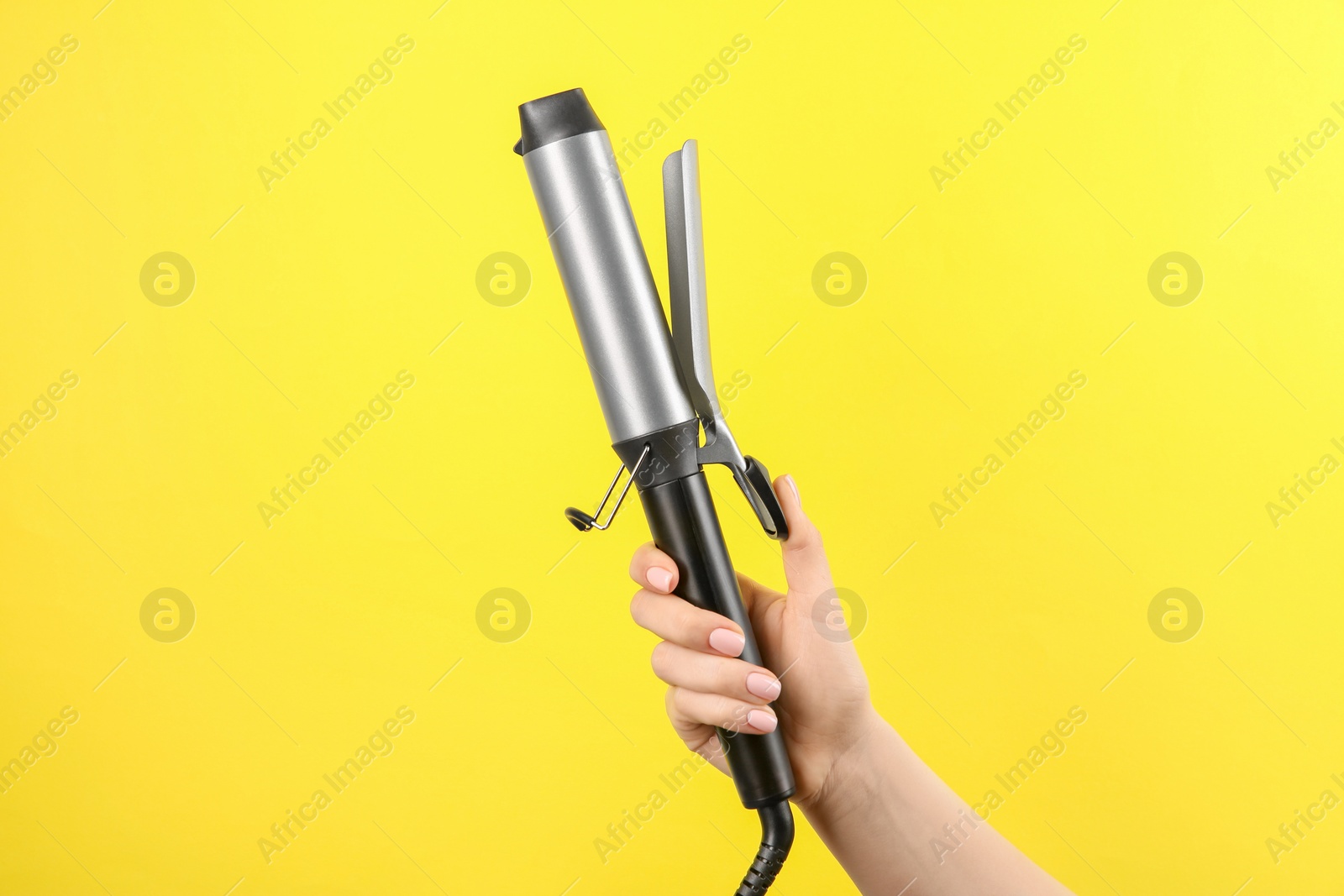 Photo of Hair styling appliance. Woman holding curling iron on yellow background, closeup