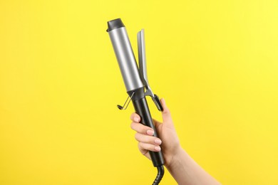 Hair styling appliance. Woman holding curling iron on yellow background, closeup