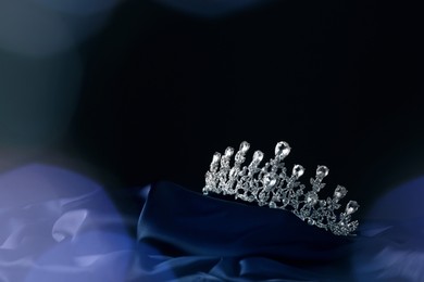 Beautiful silver tiara with diamonds on dark cloth against blurred lights, space for text