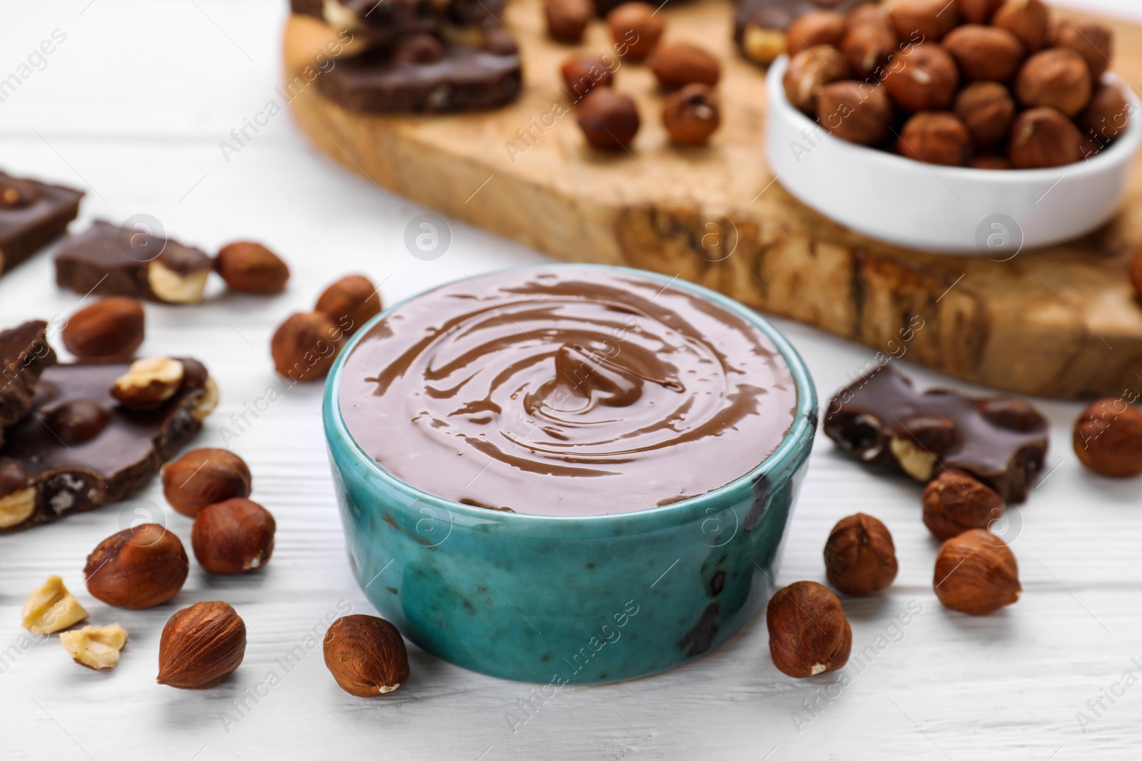 Photo of Bowl with tasty paste, chocolate pieces and nuts on white wooden table