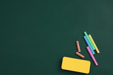 Colorful chalks and duster on green board, flat lay. Space for text