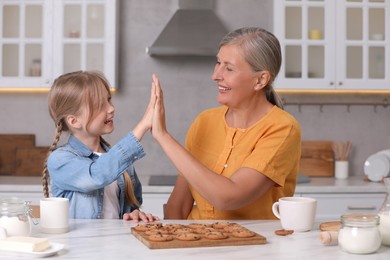 Photo of Happy grandmother giving high five to her granddaughter in kitchen