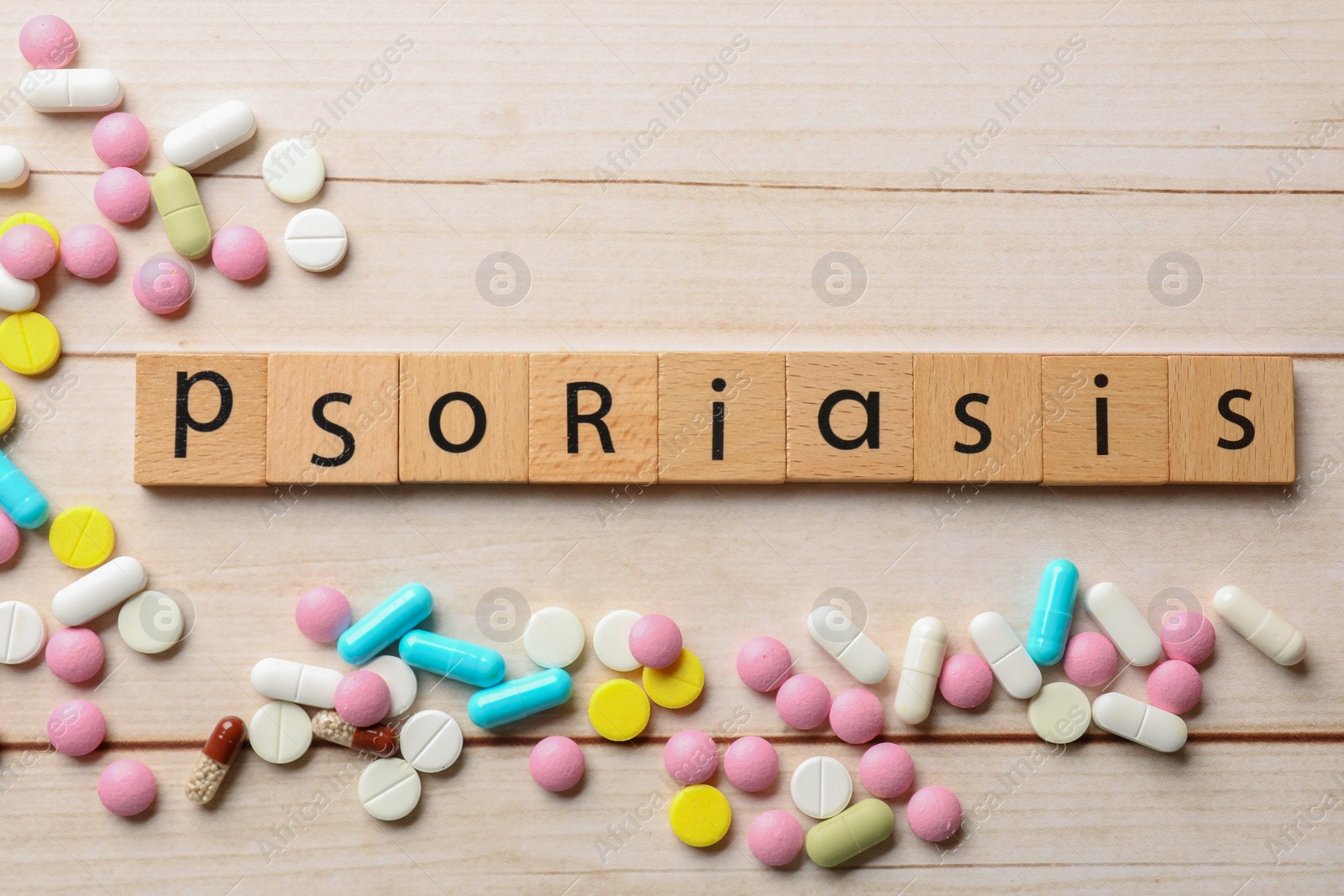 Photo of Word Psoriasis made of squares with letters and different pills on white wooden table, flat lay