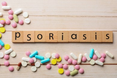 Word Psoriasis made of squares with letters and different pills on white wooden table, flat lay