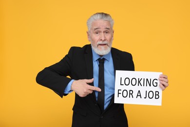 Photo of Unemployed senior man pointing at cardboard sign with phrase Looking For A Job on yellow background