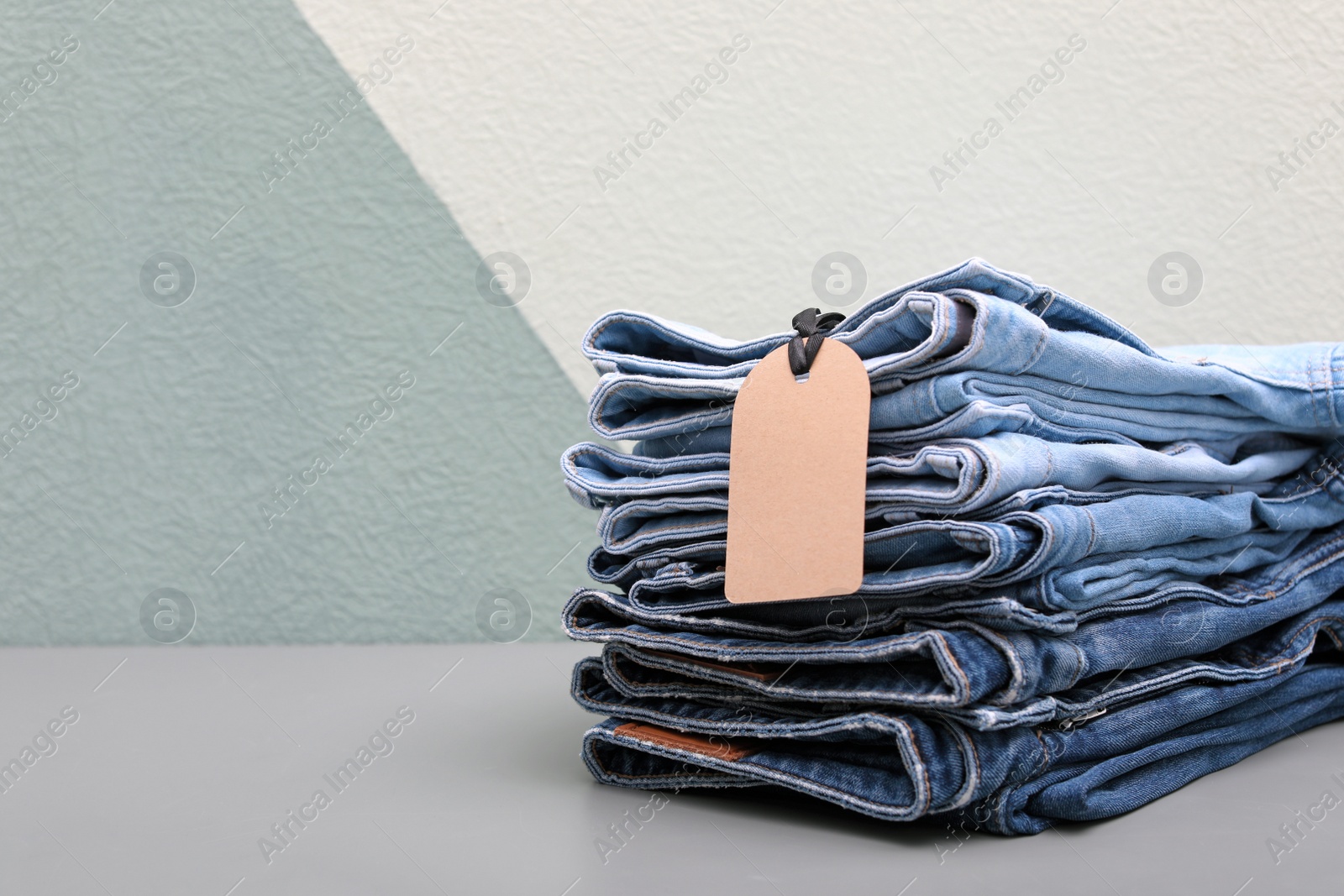 Photo of Stack of stylish jeans with tag on table against color wall