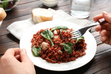 Photo of Woman eating tasty brown rice at wooden table, closeup