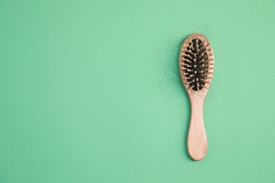 Photo of Wooden brush with lost hair on green background, top view. Space for text