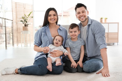 Photo of Happy couple with children sitting on floor at home. Family weekend