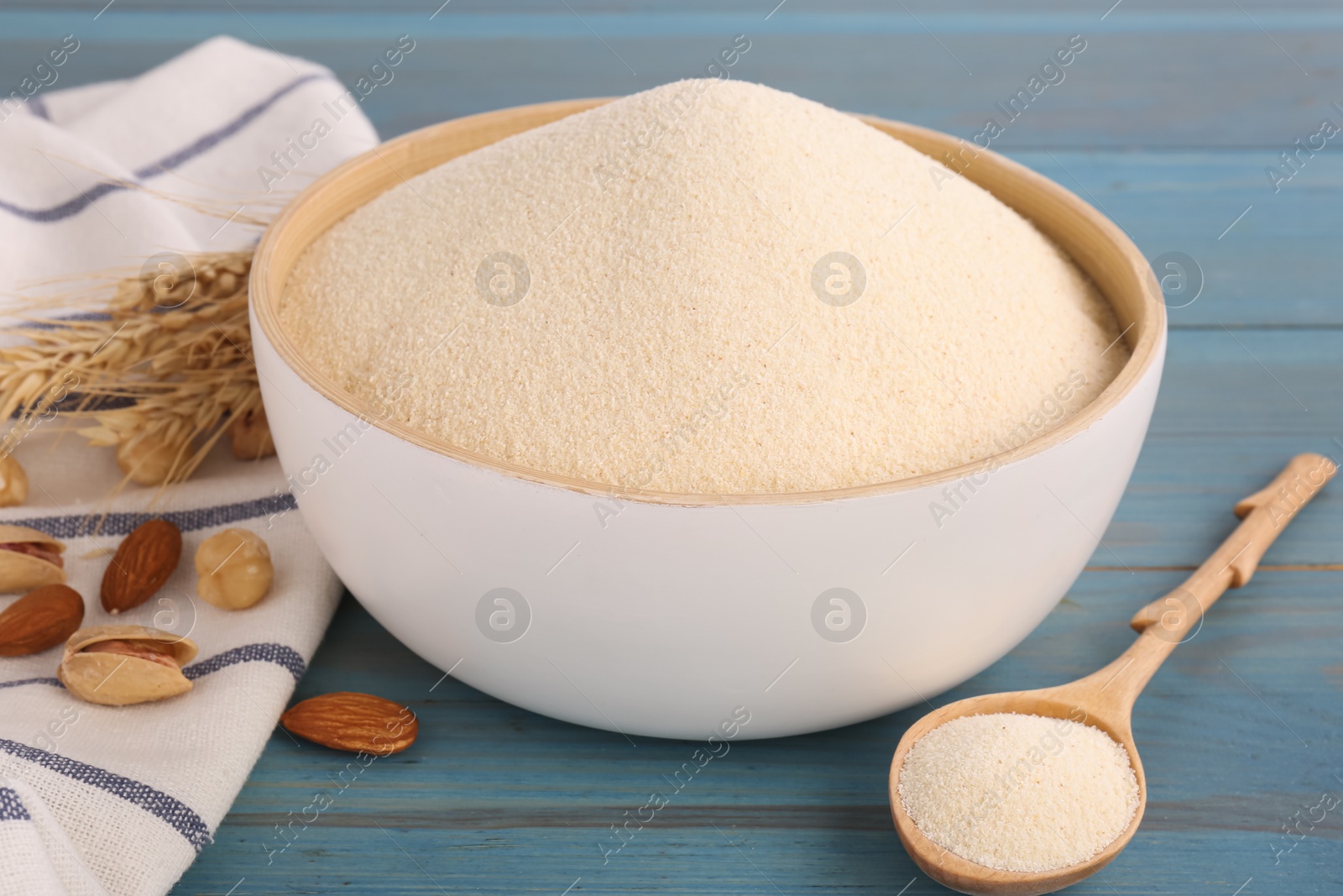 Photo of Uncooked organic semolina, spikelets and different nuts on light blue wooden table