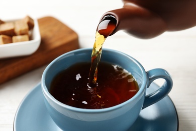 Photo of Pouring black tea into ceramic cup on wooden table