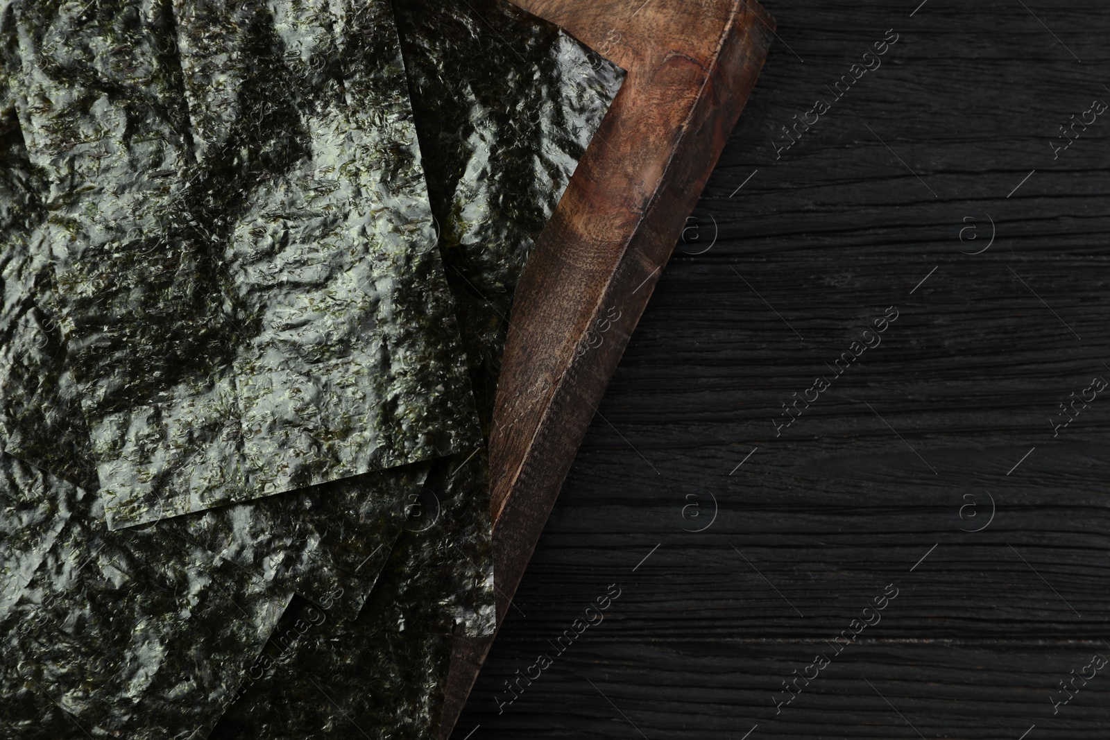 Photo of Wooden board with dry nori sheets on black table, top view. Space for text