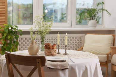 Photo of Clean dishware, flowers, fresh pastries and burning candles on table in stylish dining room