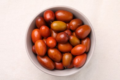 Fresh Ziziphus jujuba fruits in bowl on white tablecloth, top view