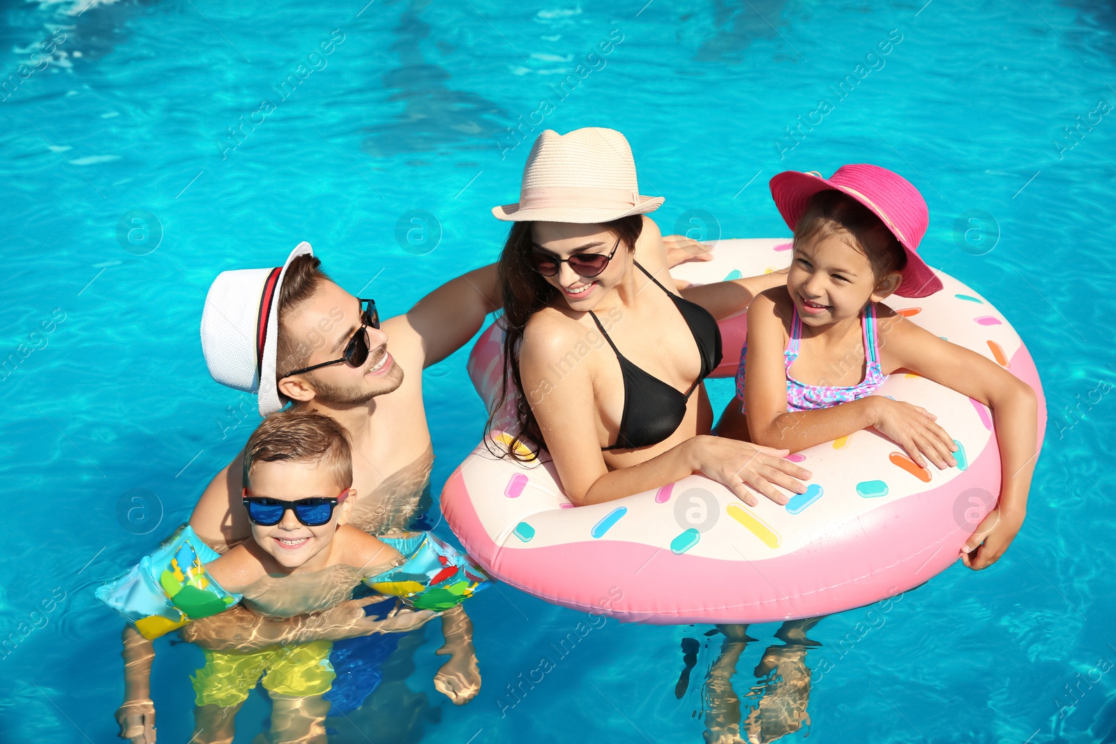 Photo of Young family with little children in swimming pool on sunny day