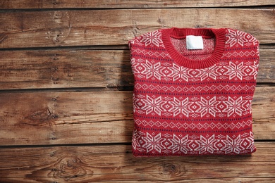 Photo of Christmas sweater with pattern and space for text on wooden background, top view