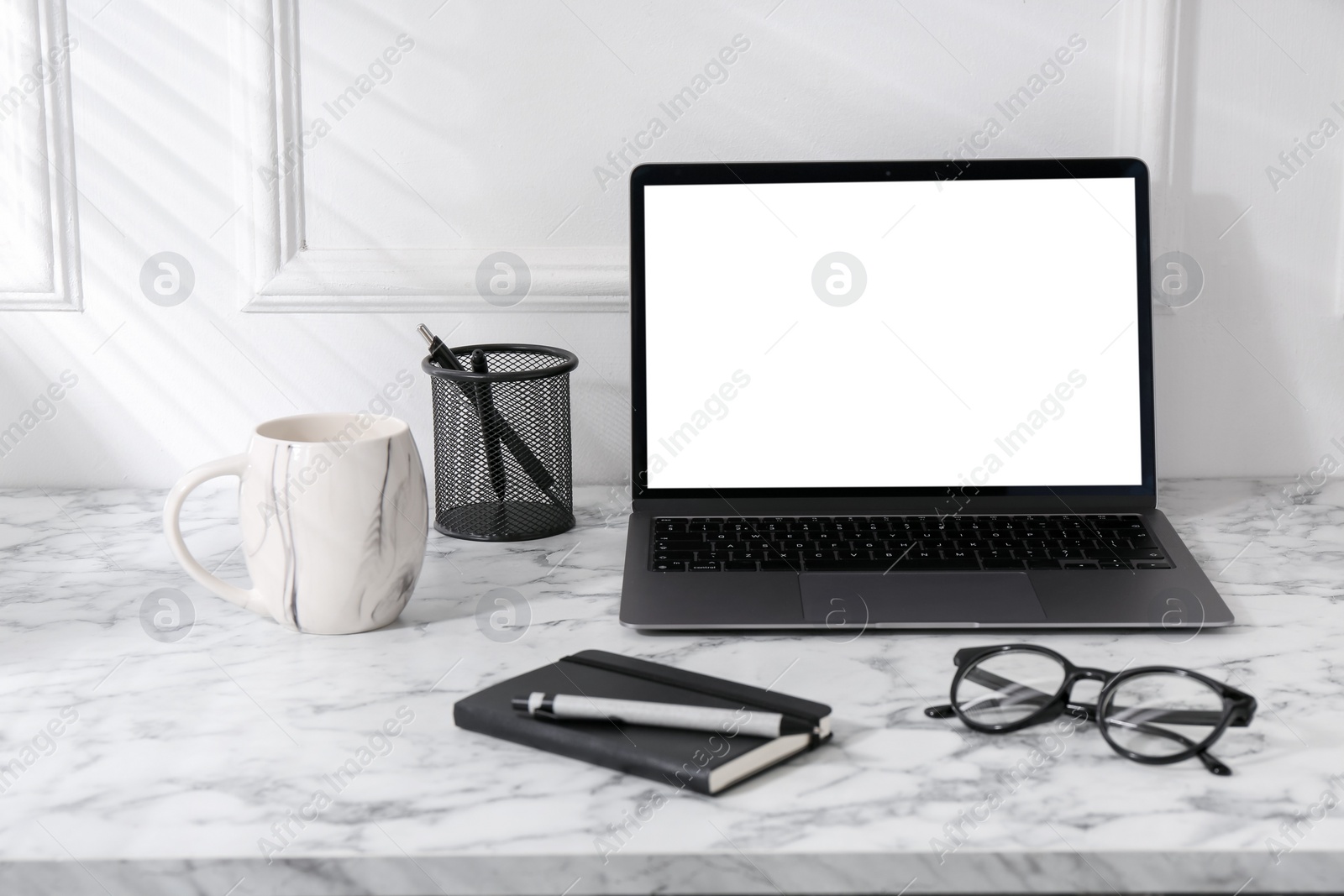 Photo of Office workplace with computer, glasses, cup and stationery on marble table near white wall