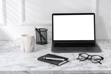 Photo of Office workplace with computer, glasses, cup and stationery on marble table near white wall