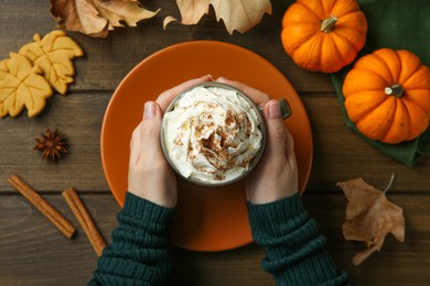 Photo of Woman holding cup of tasty pumpkin spice latte with whipped cream at wooden table, top view