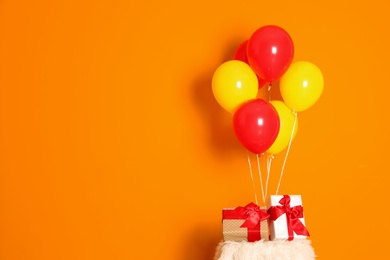 Photo of Bunch of bright balloons and gifts on table against color wall, space for text