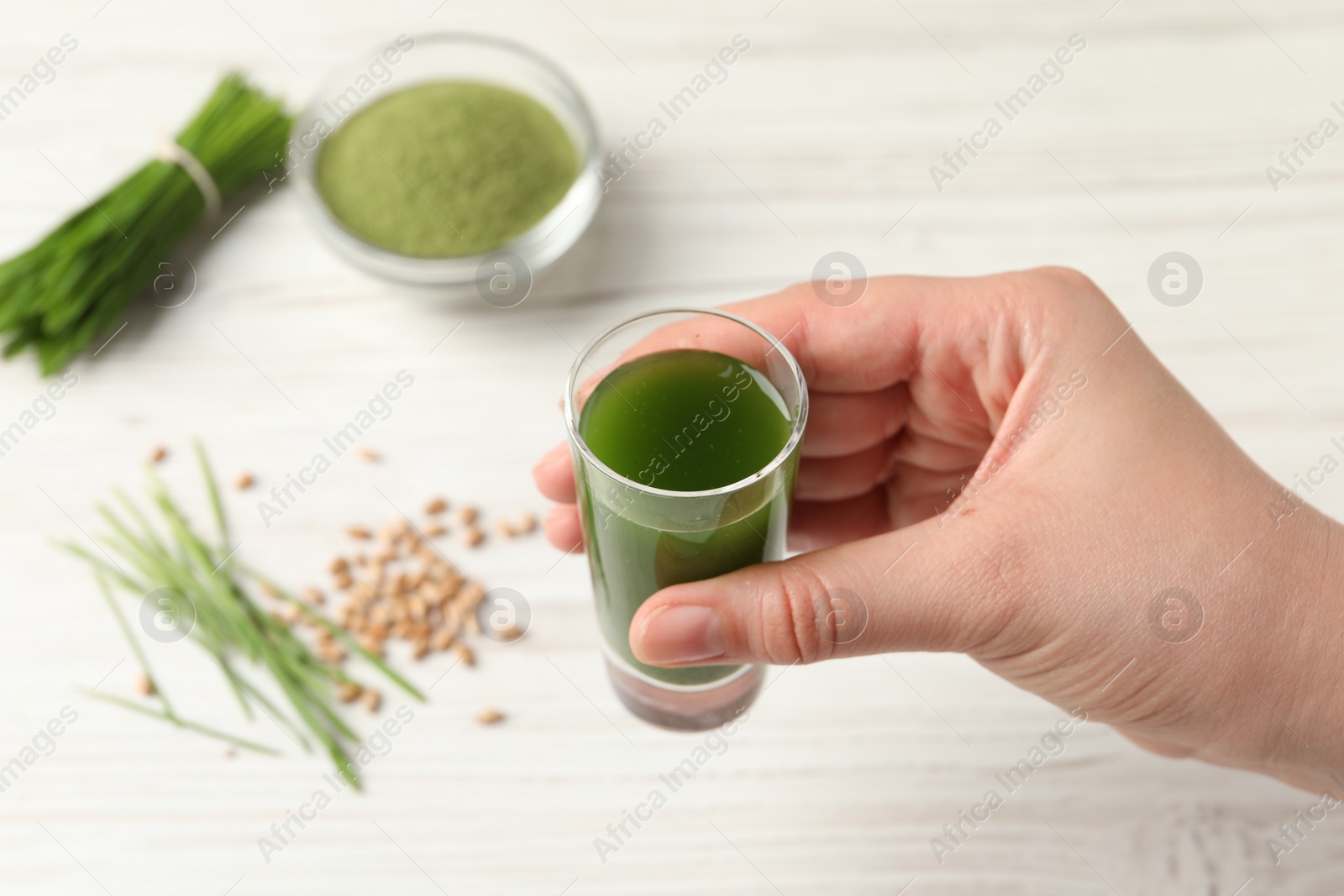 Photo of Woman holding glass of wheat grass drink at white table, closeup