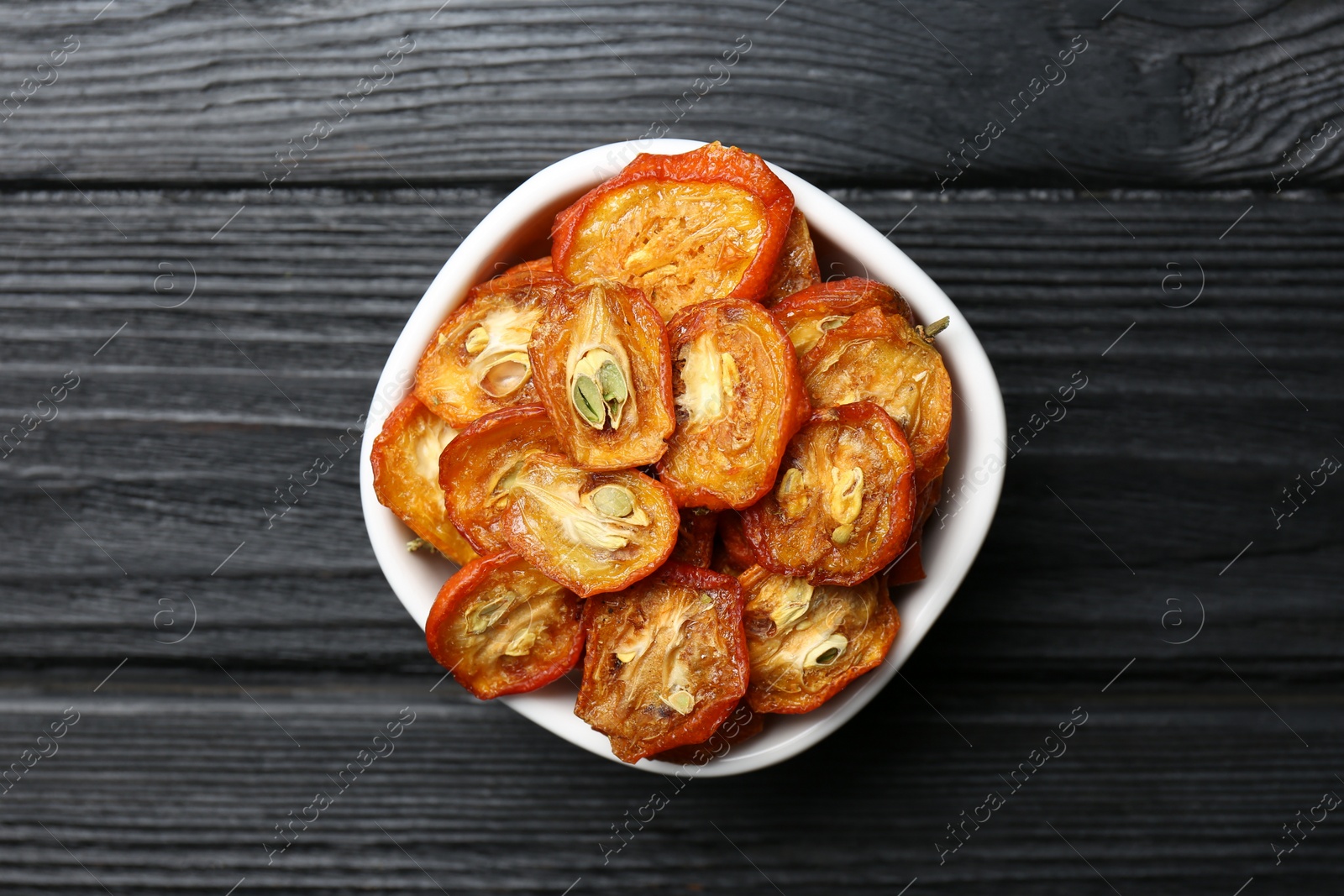 Photo of Bowl with cut dried kumquat fruits on black wooden table, top view