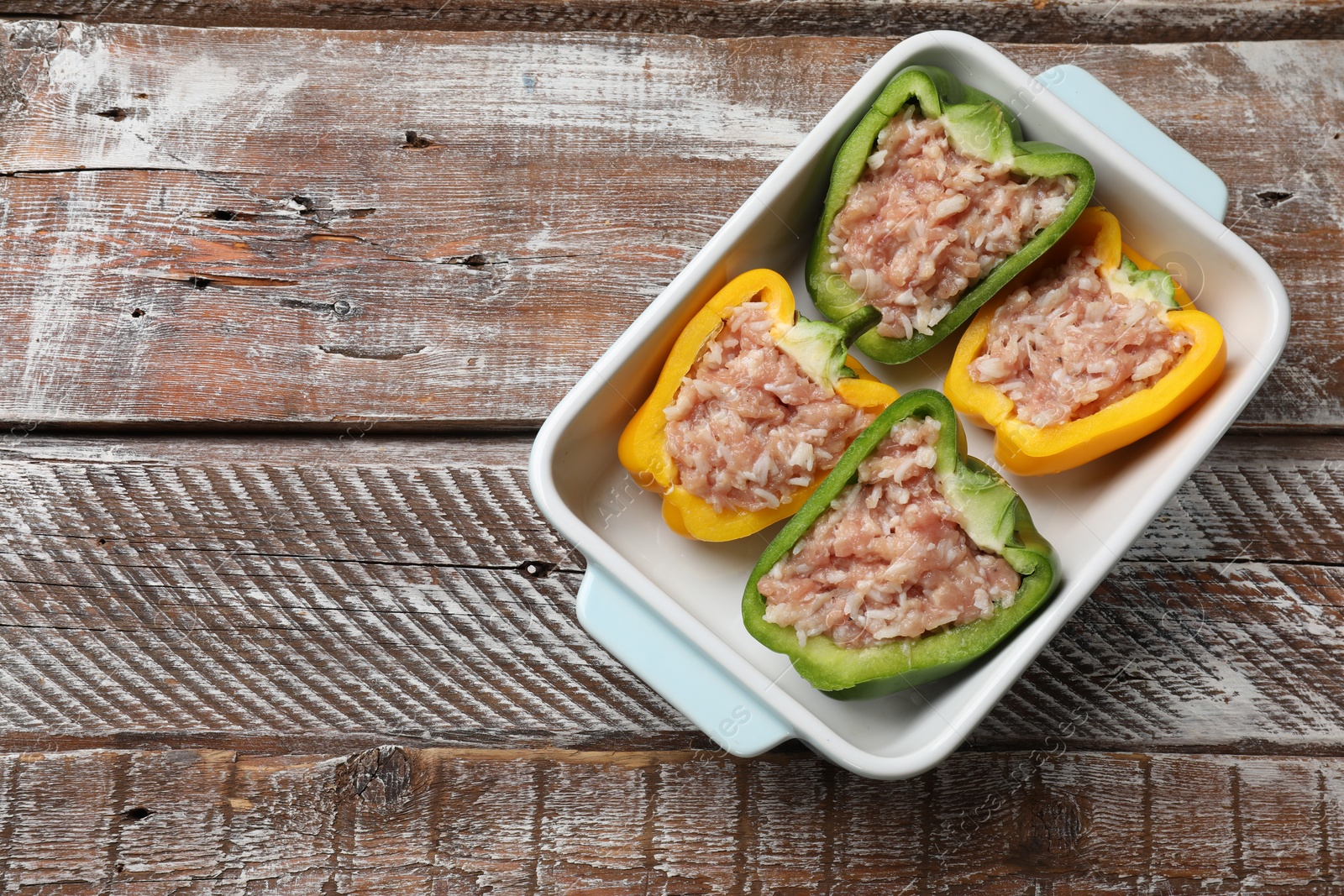 Photo of Raw stuffed peppers in dish on wooden table, top view. Space for text