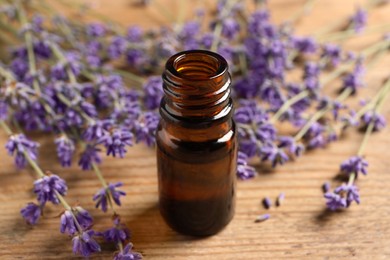 Photo of Bottle of essential oil and lavender flowers on table, closeup