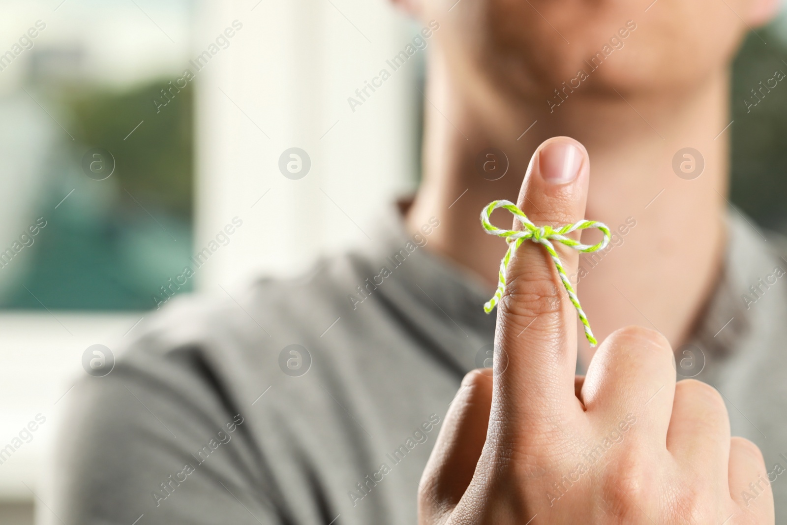 Photo of Man showing index finger with tied bow as reminder against blurred background, focus on hand