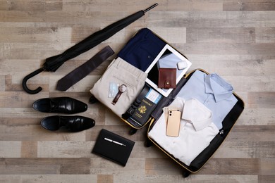 Photo of Packed suitcase with business trip stuff on wooden surface, flat lay