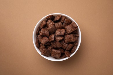 Photo of Chocolate cereal pads in bowl on brown table, top view