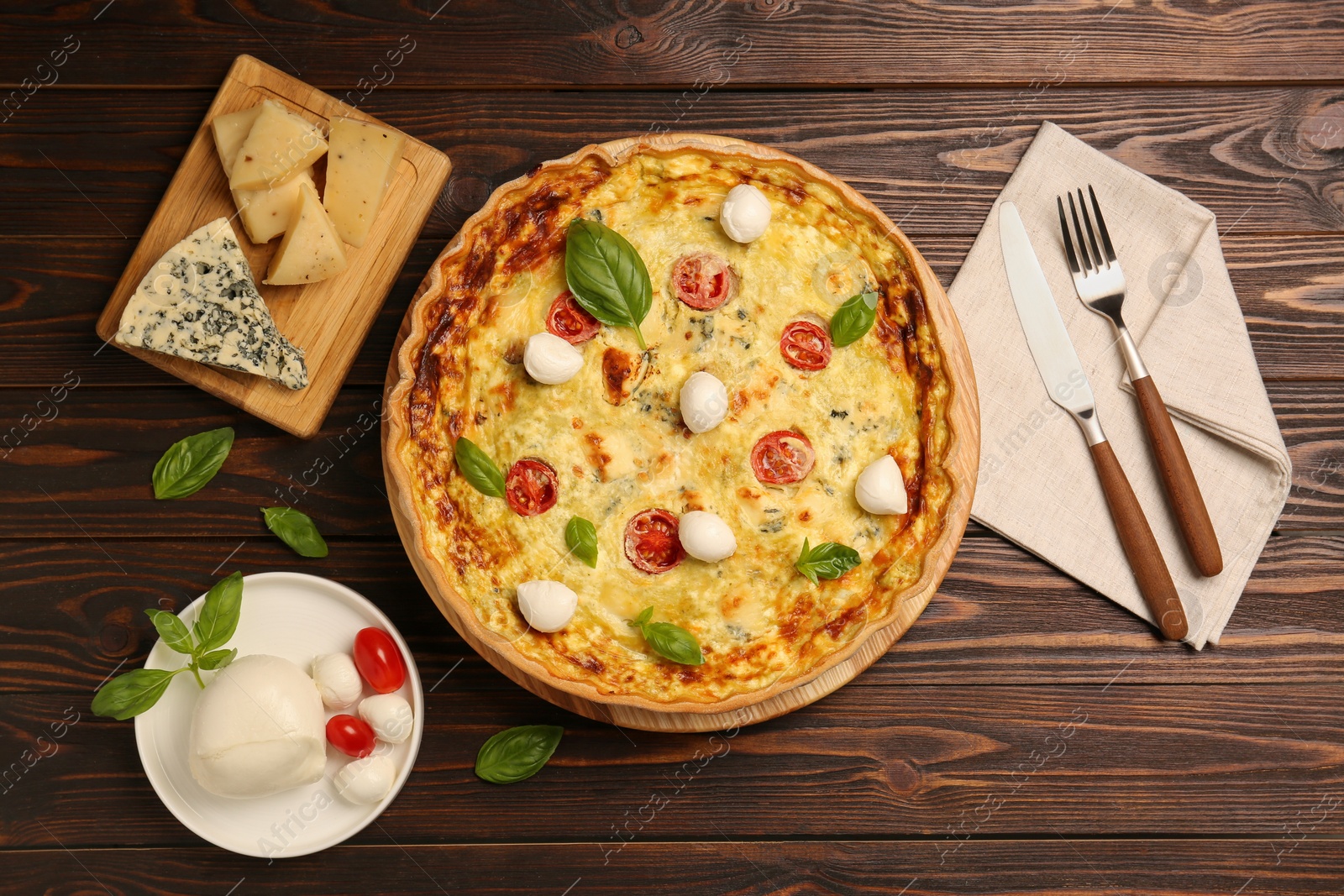 Photo of Delicious quiche with mozzarella cheese, tomatoes and basil on wooden table, flat lay