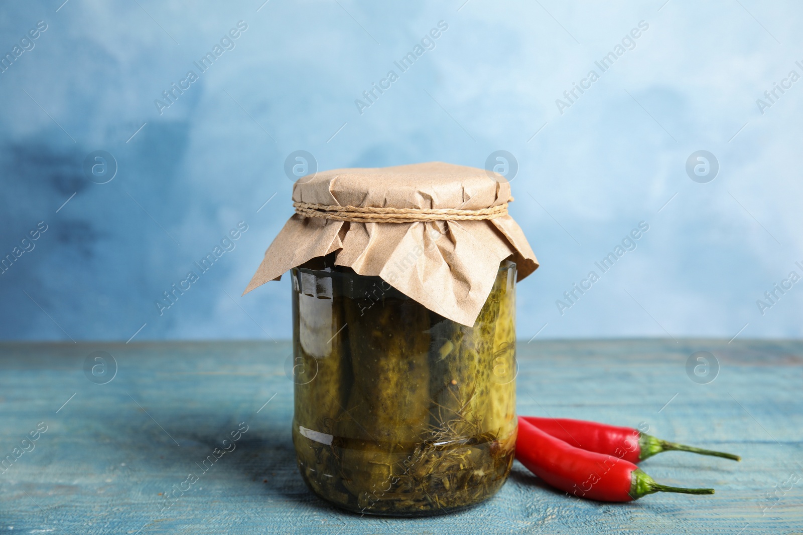 Photo of Jar with pickled cucumbers on wooden table against blue background