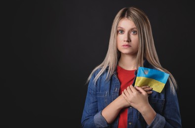 Photo of Sad woman holding Ukrainian flag on black background. Space for text