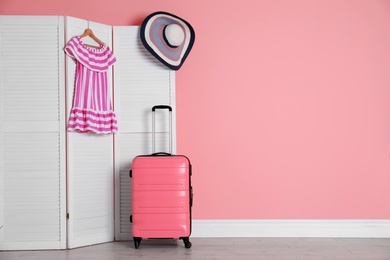 Photo of Suitcase near wooden screen with dress and hat indoors. Space for design