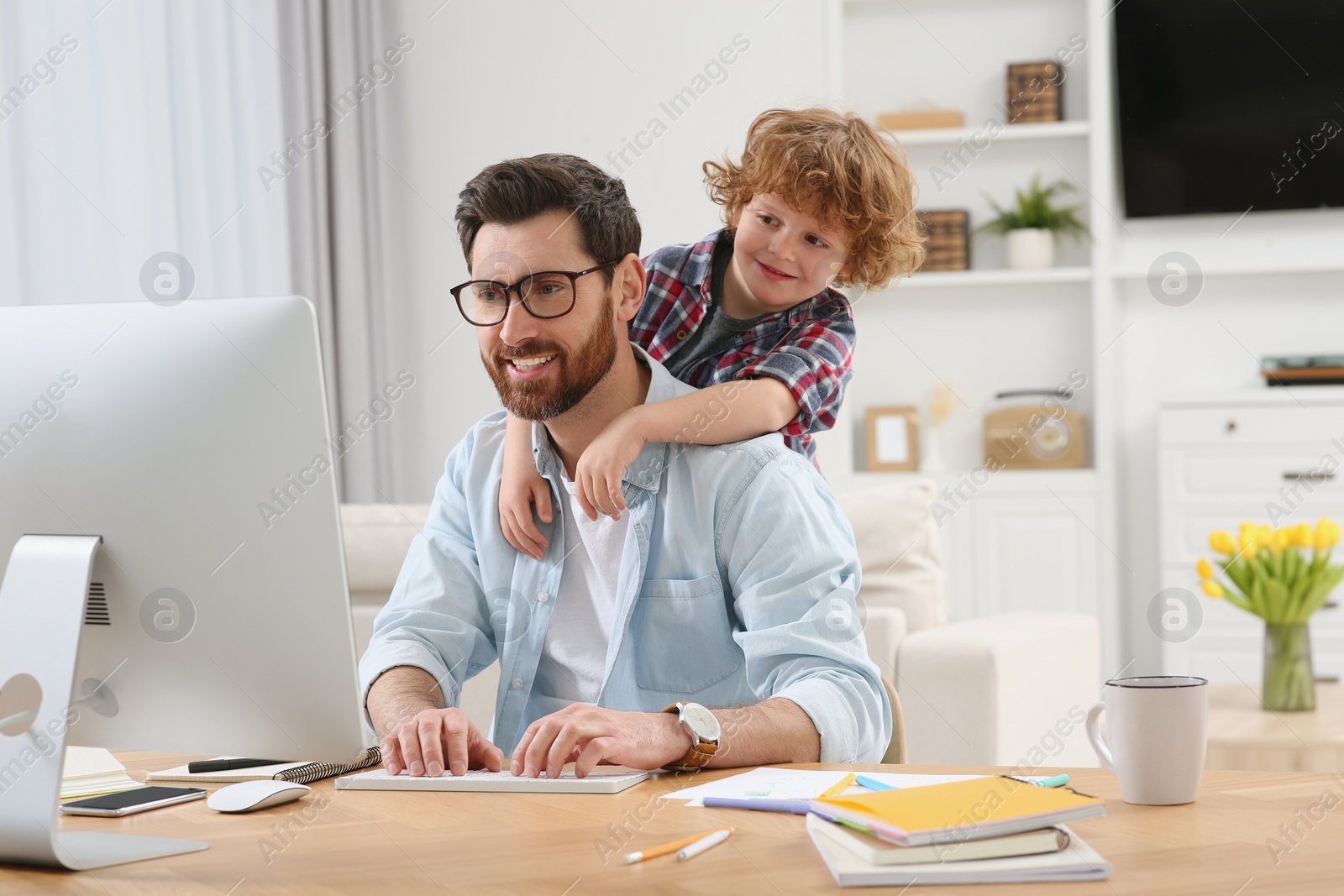 Photo of Man working remotely at home. Father with his child at desk