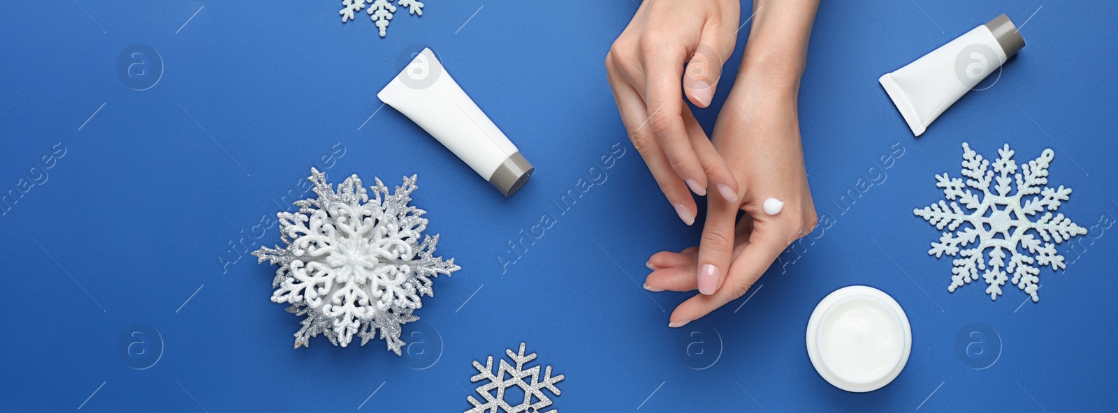 Image of Woman applying cream onto hand on blue background, top view. Banner design