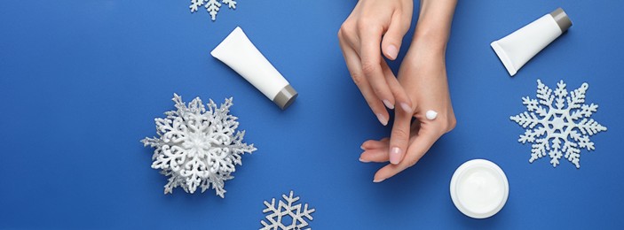 Image of Woman applying cream onto hand on blue background, top view. Banner design
