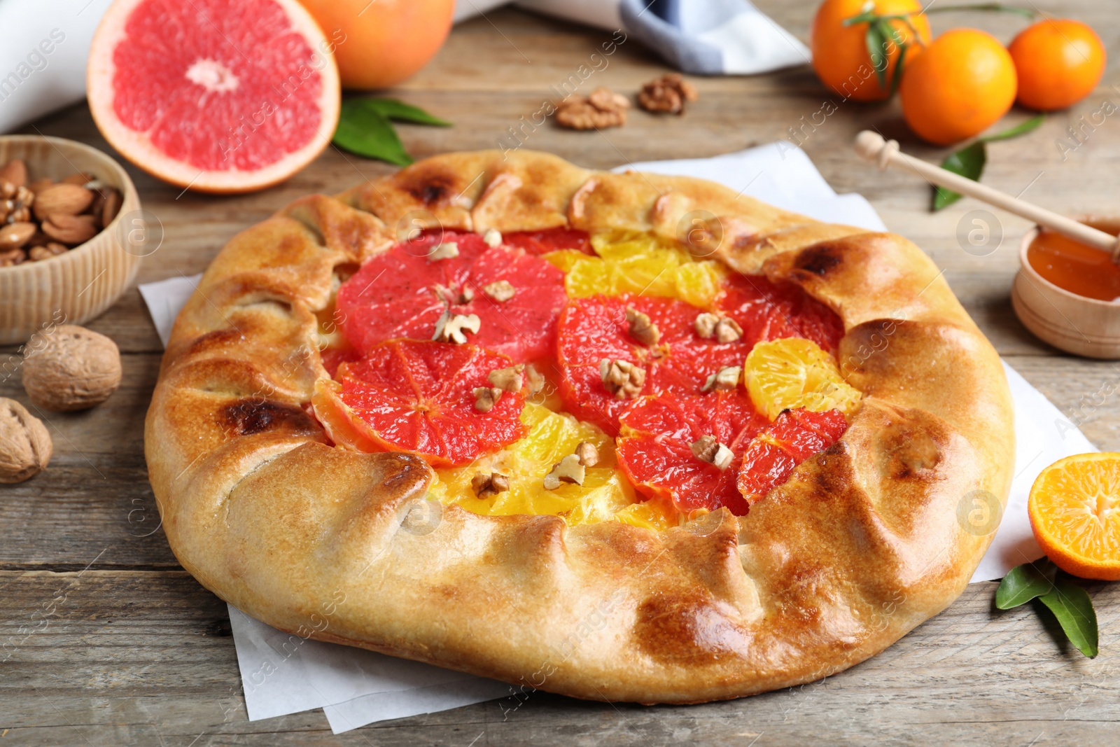 Photo of Delicious galette with citrus fruits and walnuts on wooden table, closeup