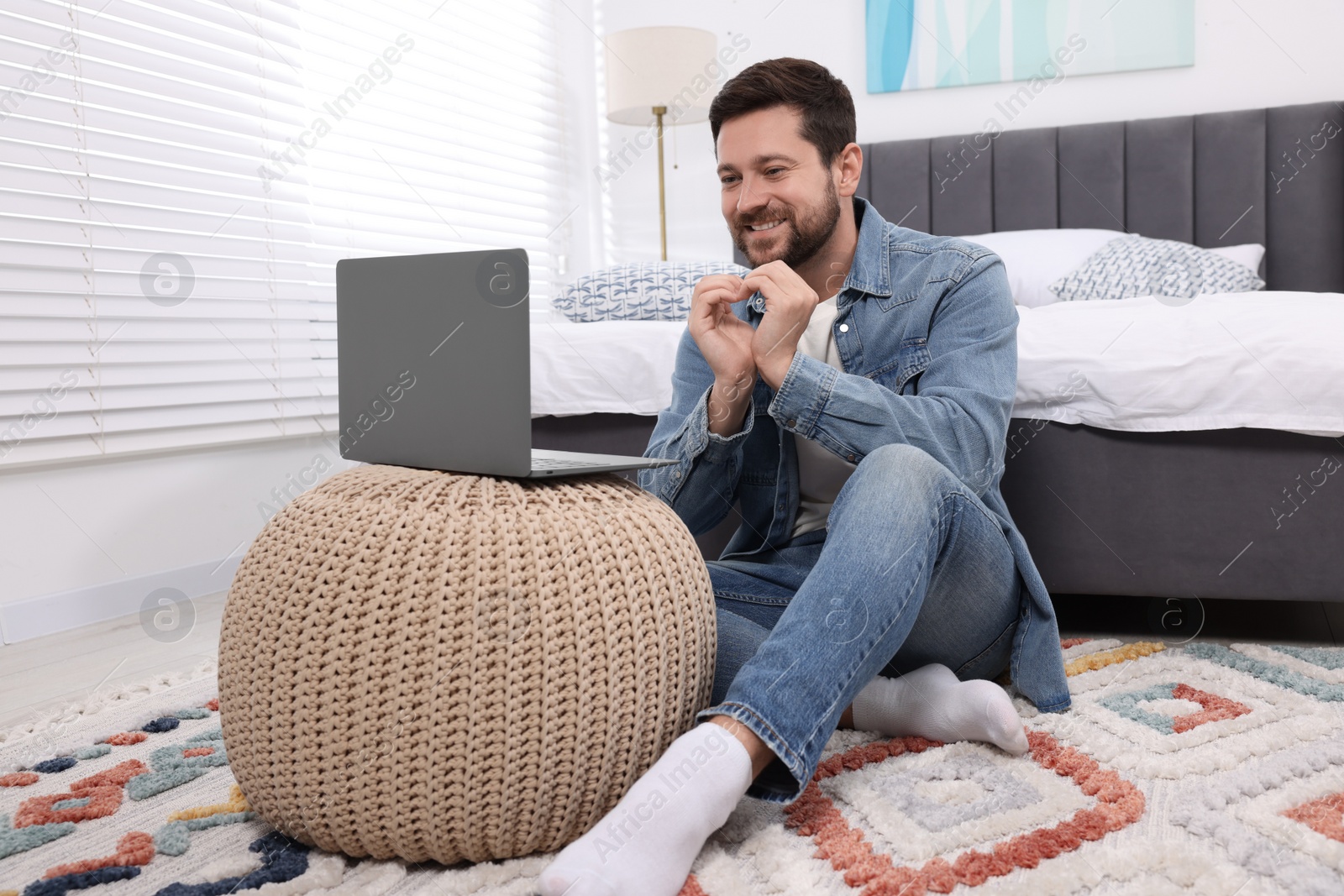 Photo of Happy man making heart with hands during video chat via laptop at home. Long-distance relationship