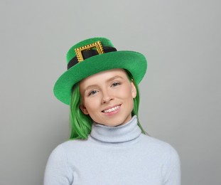 St. Patrick's day party. Pretty woman with green hair and leprechaun hat on grey background