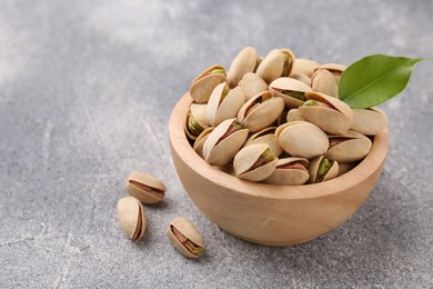 Photo of Delicious pistachios in bowl on grey textured table