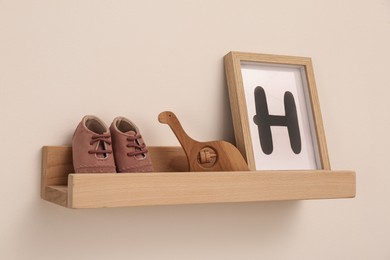 Photo of Wooden shelf with baby booties, toy and frame in room. Interior design