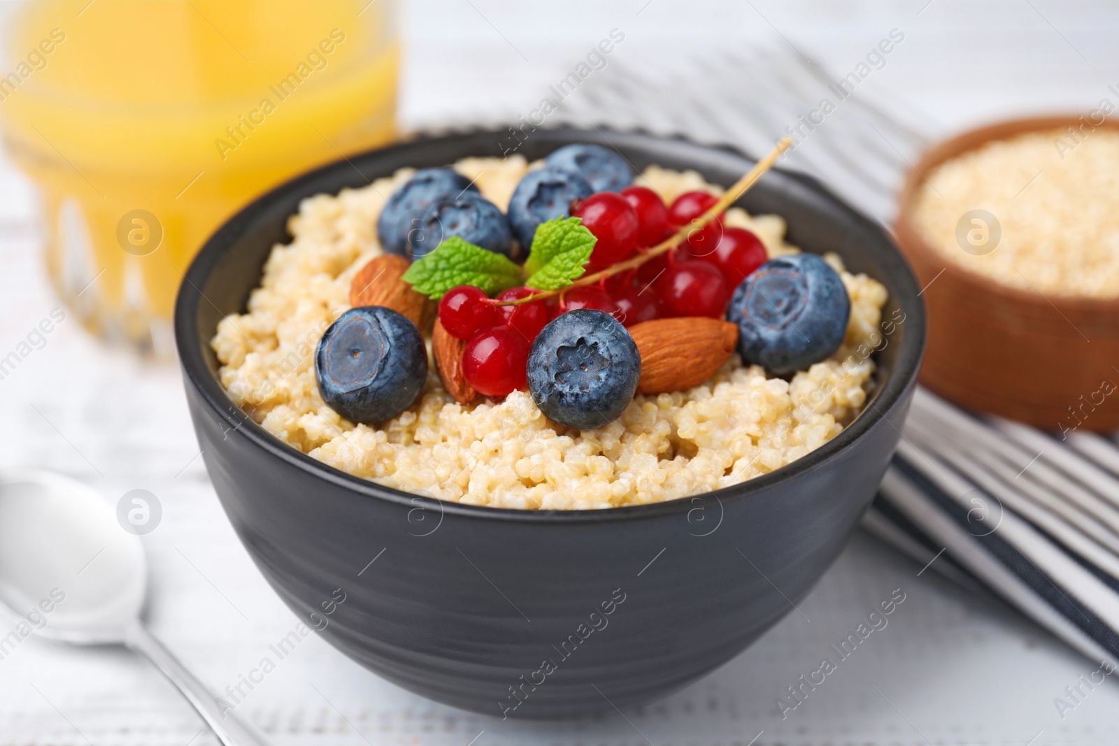 Photo of Bowl of delicious cooked quinoa with almonds, cranberries and blueberries on white wooden table, closeup