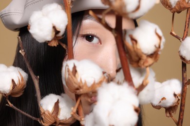 Photo of Beautiful young Asian woman with cotton branches on beige background, closeup