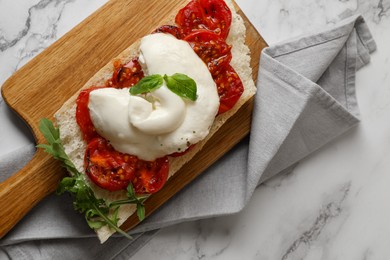 Photo of Toast with delicious burrata cheese, tomatoes and arugula on white marble table, top view