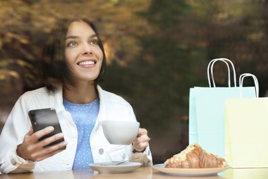 Special Promotion. Happy young woman with cup of drink using smartphone in cafe, view from outdoors