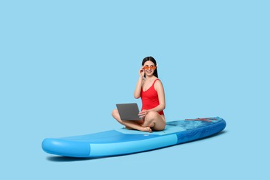 Happy woman with laptop on SUP board against light blue background